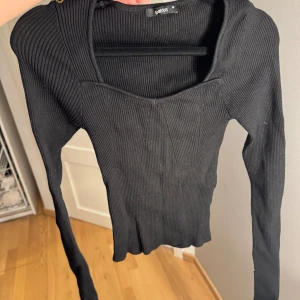 Svart ribbad långärmad tröja från Gina Tricot - Supersnygg svart ribbad tröja från Gina Tricot med lång ärm och fyrkantig urringning. Tröjan är tight i modellen och har stretchigt material som sitter perfekt. Perfekt till jeans eller kjol för en clean look. ett hål vid ärmarna vilket inte syns när man har på. den har slits vid ärmarna 