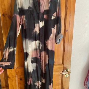 Mönstrad långklänning från Dedicated - Snygg långklänning från Dedicated i Tencel/lyocell med coolt abstrakt mönster i svart, beige, rosa och grå toner. Klänningen har långa ärmar, knappar hela vägen och två bröstfickor. Perfekt för dig som gillar unika plagg med avslappnad passform.