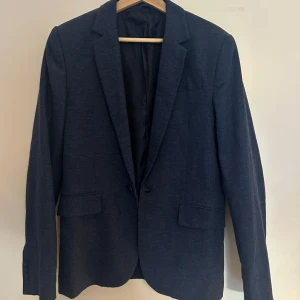 Mörkblå kavaj med klassisk passform - Snygg mörkblå linne kavaj med klassisk krage och två fickor framtill. Enkelknäppt modell med diskreta knappar vid ärmslut. Perfekt för dig som vill ha en ordentlig kavaj som passar året runt