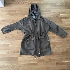 Grå parkajacka från Cellbes med huva - Säljer en grå parkajacka från Cellbes med huva och snyggt mönstrat innerfoder. Jackan har dragsko i midjan, stora fickor med knappar och dragkedja framtill. Perfekt för dig som vill ha en stilren och praktisk jacka med coola detaljer.