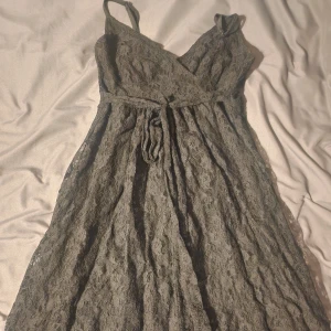 Svart spetsklänning från Lindex XS - Supersnygg lång svart klänning från Lindex i storlek XS. Klänningen har smala axelband, omlottliv och ett bälte i midjan. Hela klänningen är täckt av vacker spets och har en flowy känsla. Perfekt för dig som vill sticka ut med en elegant look.