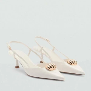 Vita klackar med gulddetalj från Mango - Stilrena vita pumps från Mango med spetsig tå och låg klack. Skorna har en  guldfärgad detalj framtill och smala remmar med spänne runt hälen. De är helt oanvända och endast testade 1 gång 🥰