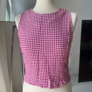 Rutig ärmlös topp i bomull - Superfin ärmlös topp i rödvitt rutigt mönster, sydd i 100% bomull. Toppen har rund halsringning, knappar längs hela ryggen och små slitsar i nederkanten. Perfekt för dig som gillar retrovibbar och vill ha något unikt till sommaren!