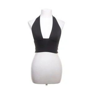 Svart halterneck croppad topp - Svart croppad halterneck topp med djup v-ringning och bred resår under bysten. Snygg minimalistisk design som knyts i nacken och lämnar ryggen bar. Perfekt för att skapa en cool och trendig look.