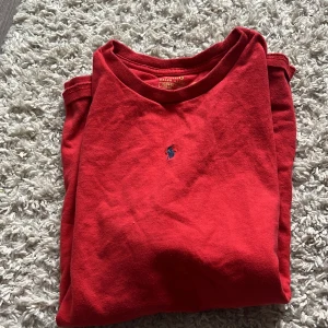 Röd tröja från Polo Ralph Lauren - Röd tröja från Polo Ralph Lauren med klassisk rund halsringning och den ikoniska broderade loggan på bröstet. Tillverkad i mjuk bomull, perfekt för en avslappnad och stilren look. Original 690 och ett annat tyg 