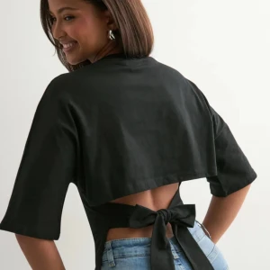 Svart topp med knyt från Nelly - Svart topp från Nelly med vida korta ärmar och snygg öppen rygg som knyts med en bred rosett. Tillverkad i mjuk bomull, perfekt för en trendig och avslappnad look. Enkel att styla med jeans eller kjol. Använd ett fåtal gånger, nypris 249kr men säljer för 120kr!