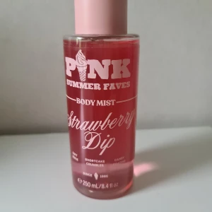 PINK Strawberry Dip Body Mist 250ml - Söt body mist från PINK i doften Strawberry Dip. Flaskan är cylinderformad i genomskinligt rosa plast med ljusrosa lock. Doften har inslag av jordgubb, shortcake crumbles och godis. Volymen är 250 ml. Vegansk och dermatologiskt testad. Helt ny och oanvänd. Alla mina produkter säljs genom köp nu, inga förhandlingar 