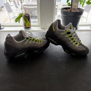 Nike Air Max 95 OG Neon Grå/Gul - Nike Air Max 95 OG i grått och svart med neongula detaljer. Ikonisk vågig design, mesh och mocka i ovandelen, synlig Air-dämpning i sulan och vita snören. Perfekt för dig som gillar retrovibbar och streetstyle. Låda följer med!