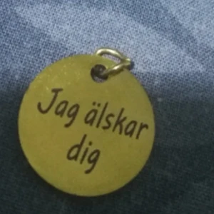 Guldigt halsbandshänge med text - Runt hänge i guldfärgad metall med texten 'Jag älskar dig' ingraverat på framsidan. Perfekt att sätta på ett halsband och ge bort till någon du tycker om. Enkel och stilren design med en liten ögla för kedja.