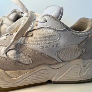 Sneakers från Gant  - Snygga sneakers från Gant i vitt och ljusgrått. Ovandel i mesh, mocka och skinn med coola paneler och broderad logga. Kraftig sula med mönstrad undersida för extra grepp. Perfekta för dig som gillar sportig och trendig stil.