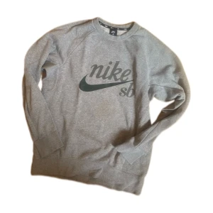 Grå Nike SB sweatshirt med logga - Snygg grå sweatshirt från Nike SB med stor svart logga framtill. Klassisk crewneck-modell med långa ärmar och ribbade muddar. Perfekt för dig som gillar streetwear och skate. Mjuk och skön bomullsblandning.