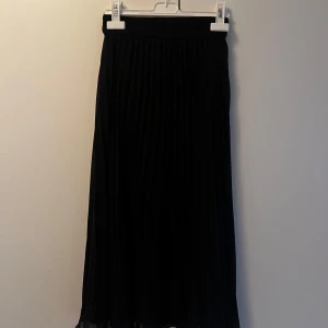 Svart plisserad långkjol från Monki - Svart plisserad långkjol från Monki i storlek XXS. Kjolen har resår i midjan och är gjord i ett lätt, flowy material som ger snyggt fall. Kjolens resorband är lite snurrat men det har inte synts när jag haft den. Katt finns i hemmet, kontakta vid fler frågor🌷