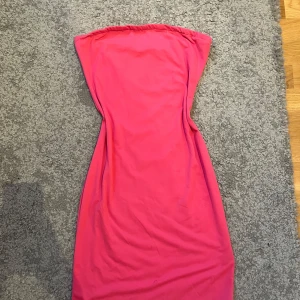 Axelbandslös rosa klänning - Snygg axelbandslös rosa klänning med figurnära passform. Perfekt för dig som vill sticka ut med en enkel men färgstark look. Klänningen är kort och har en stilren design utan detaljer eller mönster.