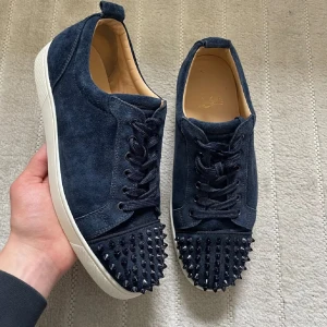 Mörkblå mocka sneakers med nitar - Snygga mörkblå sneakers i mocka från Christian Louboutin med nitar på tån. Skorna har rund tå och klassisk snörning. Perfekta för dig som vill sticka ut med en edgy vibe och exklusiv känsla.