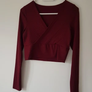 Vinröd omlottopp från SHEIN strl M - Säljer en vinröd croppad omlottopp från SHEIN med långa ärmar. Toppen är ribbad och har en snygg v-ringning framtill. Perfekt att matcha med höga jeans eller kjol för en trendig look.  Helt & fint skick dock små noppror
