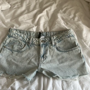 Ljusblå jeansshorts från Divided - Snygga ljusblå jeansshorts från H&M i klassisk femficksmodell. Shortsen har råa, fransiga benslut och normal passform. Perfekta för varma dagar och ger en avslappnad vibe. Tillverkade i mjukt denimtyg med dragkedja och knapp framtill. Medela mig för mer detaljer om det behövs. Pris kan diskuteras.
