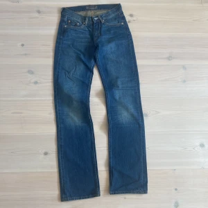 Blå jeans från Acne Jeans - Klassiska blå jeans från Acne Jeans med raka ben och snygg tvätt. Jeansen har fem fickor, silverfärgade nitar och en mörkblå läderpatch med logga bak i midjan. Perfekta för en clean och stilren look.