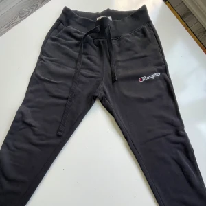 Svarta mjukisbyxor från Champion XS - Svarta mjukisbyxor från Champion i storlek XS. Byxorna har dragsko i midjan, ribbade muddar vid bensluten och Champion-logga på ena benet. Tillverkade i en mjuk bomulls- och polyestermix som är skön att ha på sig.