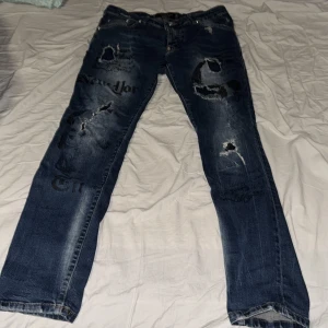 Blå jeans från Philipp Plein - Säljer ett par blå jeans från Philipp Plein med straight cut. De har slitna detaljer och tryck på framsidan som ger en cool look. Perfekta för dig som vill ha en edgy stil.
