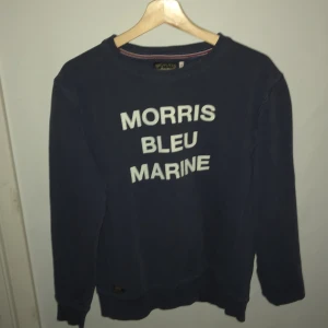 Marinblå tröja från Morris - Säljer en stilren marinblå tröja från Morris med texten 'Morris Bleu Marine' i vitt på framsidan. Tröjan har långa ärmar och en rund halsringning. Perfekt för en avslappnad och trendig look.