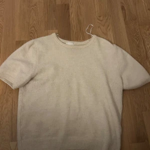 Vit stickad kortärmad tröja - Säljer en stilren vit stickad tröja med korta ärmar. Perfekt för en avslappnad look. Tröjan har en rund halsringning och ribbade kanter.