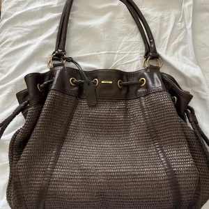 Brun axelväska  - Säljer en snygg brun axelväska från Mexx med flätat mönster och detaljer i skinn. Väskan har en praktisk dragkedja och flera fack inuti för enkel organisering. Perfekt för att bära med sig allt man behöver under dagen.