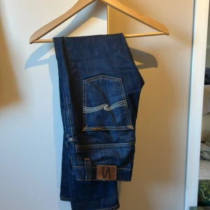 Mörkblå jeans från Nudie - Snygga mörkblå jeans från Nudie med klassisk femficksdesign och kontrastsömmar. Jeansen är i lite mer slimmade hållet och sitter ”gricsh”. Perfekta för en stilren look. Passar dig som är 170-175 