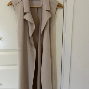 Beige väst från Zara - Snygg beige väst från Zara med knytband i midjan. Perfekt för lager-på-lager-stil och ger en elegant touch till din outfit.