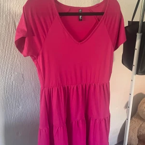 Rosa klänning från Pieces - Snygg rosa klänning från Pieces med v-ringning och korta ärmar. Perfekt för en somrig look. Klänningen har en luftig passform och är gjord i ett mjukt material.