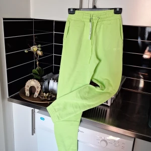 Limegröna mjukisbyxor med snörning - Snygga limegröna mjukisbyxor med elastisk midja och snörning. Perfekta för en avslappnad stil. Byxorna har ribbade muddar vid bensluten och sidofickor för extra bekvämlighet.