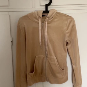 Beige hoodie med dragkedja - Säljer en mysig beige hoodie med dragkedja och huva. Tröjan har långa ärmar och praktiska fickor framtill. Perfekt för en avslappnad stil.