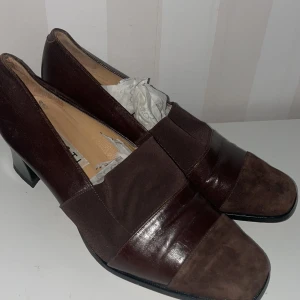 Bruna pumps från Giusti nyskick  - Eleganta bruna pumps från Giusti i skinn med en klassisk design. Skorna har en låg klack och en stilren, spetsig tå. Perfekta för en sofistikerad look.