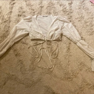 Vit knytblus från NLY One - Säljer en stilren vit blus från NLY One med långa ärmar och knytning framtill. Perfekt för en chic look med sin omlott-design och lätta material.