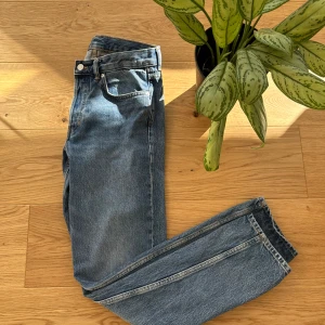 Blå jeansbyxor - Snygga blå jeansbyxor med klassisk femficksdesign och knappgylf. Perfekta för en avslappnad stil. Midjan är midwaist och passformen är straight, vilket ger en tidlös look.