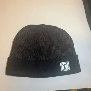Svart mössa med logotyp - Snygg svart mössa med uppvikt kant och en stilren logotyp framtill. Perfekt för att hålla värmen med stil. Prisen kan diskuteras 