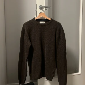 Brun stickad tröja från Casual Friday  - Säljer en stilren brun stickad tröja från Norse Projects. Tröjan har långa ärmar och en rund halsringning. Perfekt för kyligare dagar och passar bra till både jeans och chinos.