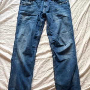 Blå jeans från Replay - Snygga blå jeans från Replay i modellen Anbass. De har en klassisk femficksdesign och en knappgylf. Perfekta för en avslappnad stil.