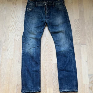Blå Diesel Jeans  - Snygga blå Diesel jeansbyxor med klassisk femficksdesign och knappgylf. De har en straight passform och är perfekta för en avslappnad stil. Slitna detaljer ger dem en cool look. Storlek W32 L32