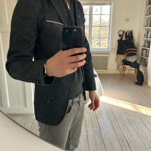 Mörkgrå kavaj - Snygg mörkgrå kavaj med smal passform och klassisk design. Kavajen har två knappar framtill och en bröstficka med vit kant. Perfekt för både formella och semi-formella tillfällen.