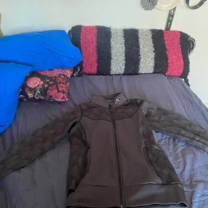 Svart flis jacka från Klim - Säljer en svart jacka från Klim med dragkedja och långa ärmar. Jackan har ett stilrent utseende med diskreta mönster på ärmarna och är perfekt för kyligare dagar. Jag har växt ut den hade den en säsong av skoter åkning, den håller värmen jätte bra när det är 15- men har även haft den under jackan i stallet när det har varit kallt. Den är inte för varm att åka med när det är 0 grader heller.