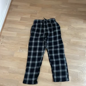 Svarta rutiga byxor - Säljer ett par svarta byxor med vitt rutmönster. Byxorna har en elastisk midja för extra komfort och är perfekta för en avslappnad stil. De är tillverkade i ett mjukt material som känns skönt mot huden.