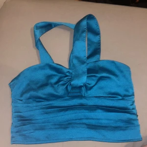 Blå korsettopp från Gina Tricot - Snygg blå korsettopp från Gina Tricot med breda axelband och rynkdetaljer framtill. Toppen har en smickrande passform och är perfekt för en kväll ute. Tillverkad i ett glansigt material som ger en lyxig känsla.