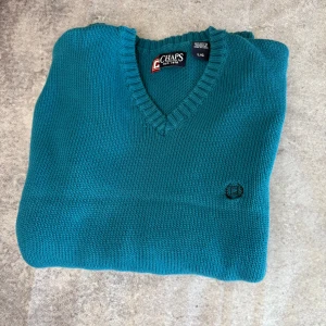 Turkos tröja från Chaps - Säljer en snygg turkos tröja från Chaps i 100% bomull. Tröjan har en v-ringad design och långa ärmar, perfekt för en stilren look. Den är ribbad vid halsringningen och har en diskret logga på bröstet.