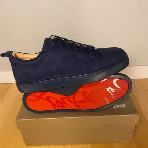  Sneakers från Christian Louboutin - Snygga mörkblå sneakers i mocka från Christian Louboutin med den ikoniska röda sulan. Skorna har snörning och en stilren design som passar perfekt för en trendig look.
