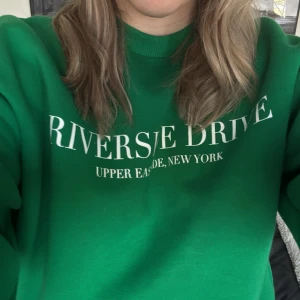 Grön sweatshirt med tryck - Snygg grön sweatshirt med texten 'Riverside Drive Upper East Side, New York' tryckt på framsidan. Perfekt för en avslappnad stil.