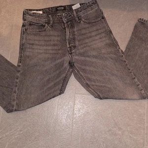 Grå jeans från Jack & Jones - Snygga grå jeans från Jack & Jones med en loose fit. De har en klassisk femficksdesign och en cool sliten detalj. Perfekta för en avslappnad stil.
