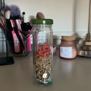 Blandade smycken i glasburk - En glasburk fylld med olika smycken, inklusive guldiga halsband och färgglada pärlor. Perfekt för den som älskar att mixa och matcha accessoarer. Burken innehåller en härlig mix av färger och stilar. det är 4 halsband, ett par örhängen, två hårspännen och ett armband🥰