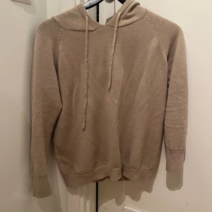 Beige merino hoodie - Säljer en stilren beige hoodie med långa ärmar och justerbar huva. Perfekt för en avslappnad look. Passar bra till både jeans och mjukisbyxor.