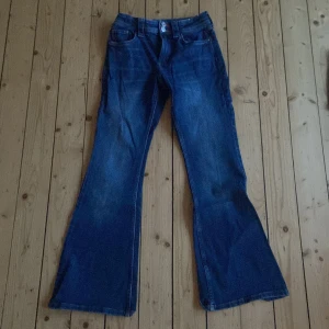 Blå utsvängda jeans från H&M - Säljer ett par coola blå jeans från H&M med utsvängda ben och justerbar midja. De har snygga stjärndetaljer på bakfickorna som ger en unik touch. Perfekta för dig som vill ha en retro look! Använt endast 1 gång säljer pga för små💕