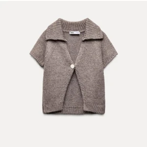 Beige stickad kofta från Zara - Säljer en mysig beige stickad kofta från Zara med korta ärmar och en stor knapp framtill. Perfekt för lager-på-lager-stil och har en ribbad krage och nederkant. Passar bra till både jeans och kjol.